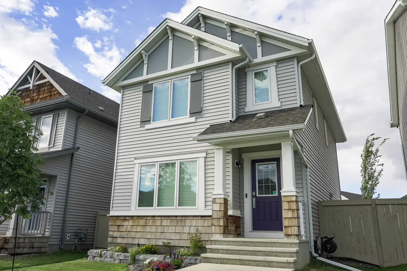 A two-story gray home with a shingle roof and shake accents