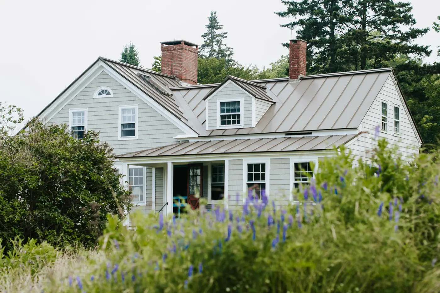 A farmhouse-style home with a standing-seam metal roof and cottage garden